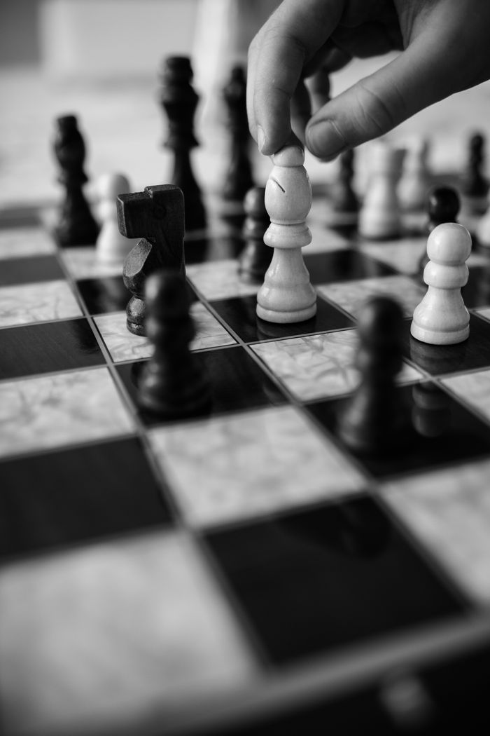 Services Black and white photo of a hand moving a chess piece on a chessboard.