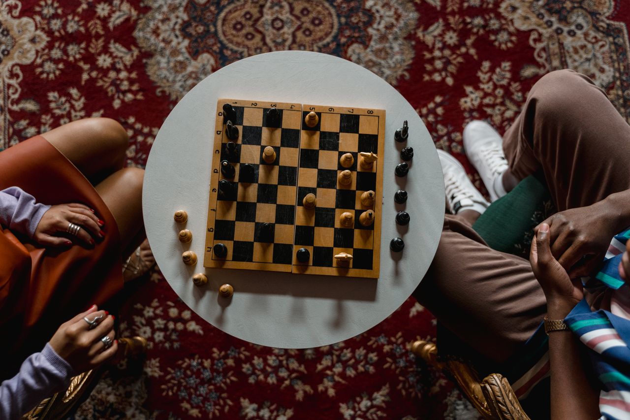 About Overhead view of a chess game between two people seated indoors, focused on strategy.